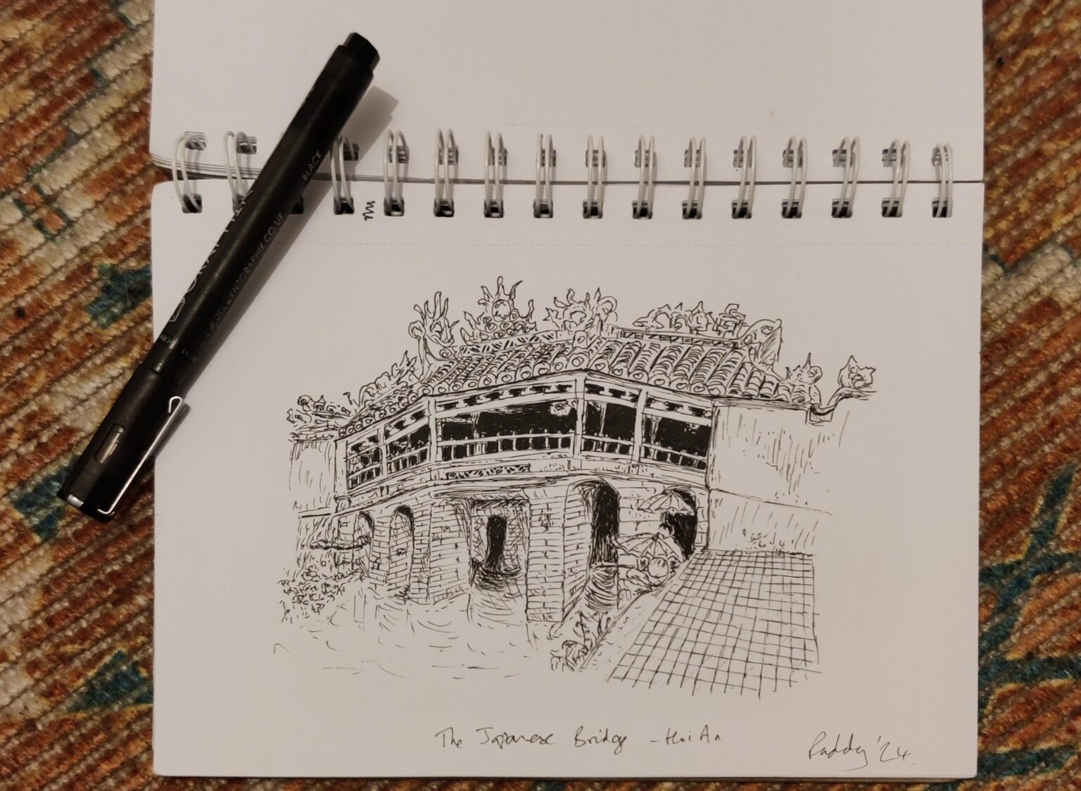 Japanese Bridge Hoi An. Fine-liner sketch Japanese Bridge Hoi An. Fine-liner sketch A sktch of 2 men holding umbrellas fishing in a river next to an ornate bridge in Hoi An.